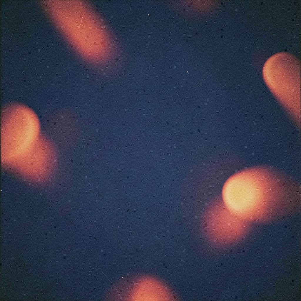 An analog film photograph with visible grain showing a deep navy blue background with soft orange-red accent shapes and subtle rounded forms, evoking a thoughtful and modern research atmosphere.