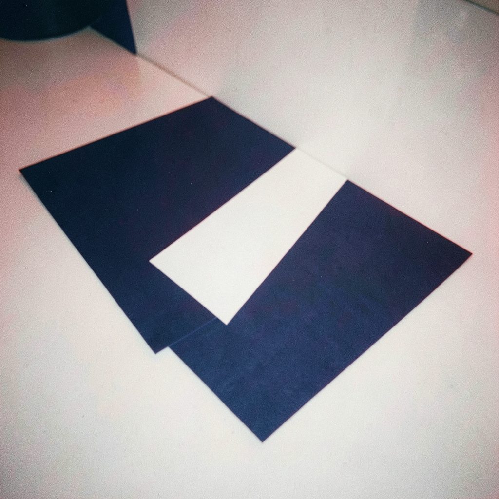 A softly lit analog film photograph with visible grain showing an abstract arrangement of navy blue and white geometric shapes overlapping on a clean surface, conveying a calm analytical mood.